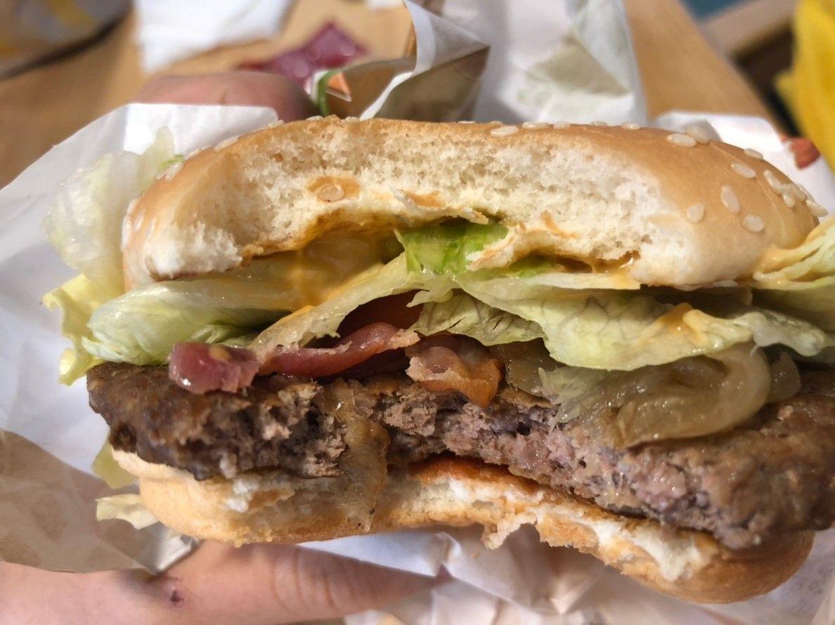 Bite taken out of a McDonald's 1955 burger in Korea showing layers with bacon and cheese.